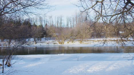 Wide-static-shot-of-a-frozen-river-surrounded-by-snow-covered-trees-in-Canada's-north