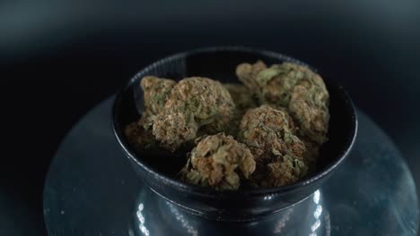 Grayish-Green-Dried-Marijuana-Buds-Close-Up-Shot,-pile-of-dried-marijuana-plants-in-a-shiny-bowl,-trichomes-strains,-on-a-reflecting-rotating-stand,-studio-lights,-cinematic-zoom-out-slow-motion