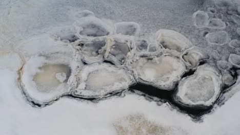 Ice-shape-and-yellow-foam-formation-float-on-dark-lake-water,-cold-winter