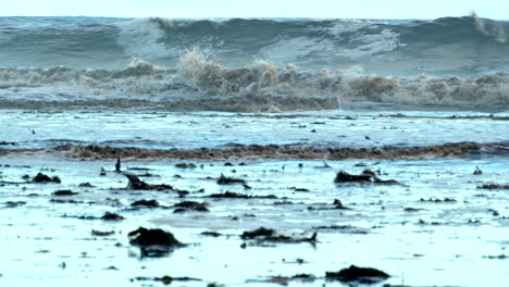 Verfärbte-Wellen,-Die-Nach-Einem-Küstensturm-Zum-Strand-Laufen,-Und-Trümmer-In-Untiefen