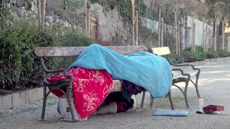 Obdachloser-Liegt-An-Einem-Kalten-Wintertag-Unter-Decken-Und-Einem-Schlafsack-Auf-Einer-Bank