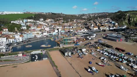 Aerial-drone-shot-of-Hastings-UK,-Pull-Away-Shot-of-amusement-park,-old-town-and-Land-Based-Fishing-Fleet