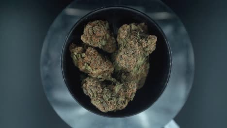 Grayish-Green-Dried-Marijuana-Buds-view-from-above-Shot,-pile-of-dried-marijuana-plants-in-a-shiny-bowl,-trichomes-strains,-on-a-reflecting-rotating-stand,-studio-lights,-zoom-in-slow-motion-120-fps