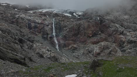 Stunning-mountain-waterfall-in-Valmalenco-Alps,-foggy-weather,-tilt-up-reveal