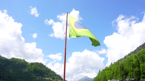 La-Bandera-Brasileña-Comienza-A-Ondear-Por-El-Viento-En-Un-Día-Soleado-Con-Nubes-En-Alleghe,-Italia.