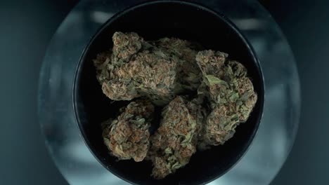 Grayish-Green-Dried-Marijuana-Buds-view-from-above,-pile-of-dried-marijuana-plants-in-a-shiny-bowl,-trichomes-strains,-on-a-reflecting-rotating-stand,-studio-lights,-rotating-slow-motion-120-fps