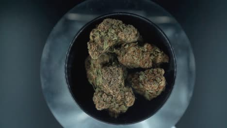 Grayish-Green-Dried-Marijuana-Buds-view-from-above-Shot,-pile-of-dried-marijuana-plants-in-a-shiny-bowl,-trichomes-strains,-on-a-reflecting-rotating-stand,-studio-lights,-slow-motion-120-fps