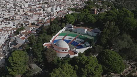 Outdoor-amphitheater-in-Mijas,-surrounded-by-white-Spanish-buildings-and-greenery,-aerial-view