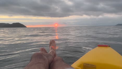 Playing-with-the-water-while-floating-with-the-kayak-in-the-middle-of-the-sea,-observing-the-sunset-and-the-islands