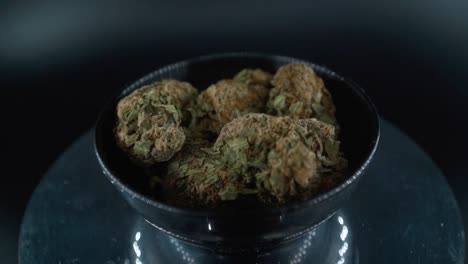 Dreamy-Green-Dried-Marijuana-Buds-Close-Up-Shot,-pile-of-dried-marijuana-plants-in-a-shiny-bowl,-trichomes-strains,-on-a-reflecting-rotating-stand,-studio-lights,-cinematic-crane-rotating-slow-motion