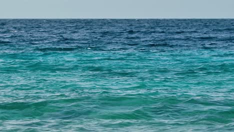 Strong-ocean-wave-current-ripples-roll-to-shore-showing-green-to-dark-deep-blue-water-gradient