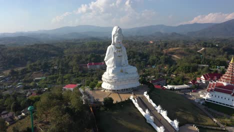 Aerial-of-Wat-Huay-Pla-Kang-giant-white-big-statue-and-pagoda-temple-with-mountains-and-landspace-in-Chiang-Rai,-Thailand