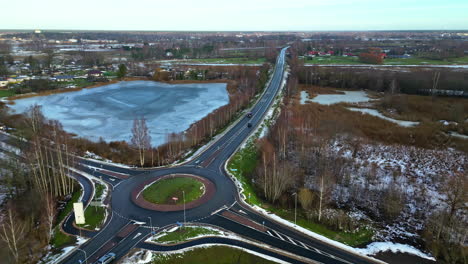 Aerial-drone-top-down-shot-over-a-road-crossing-beside-a-frozen-lake-on-a-cold-winter-day