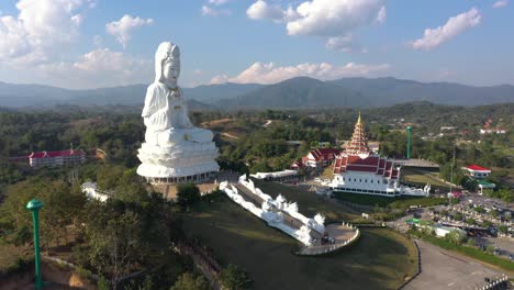Amazing-backwards-aerial-drone-of-Wat-Huay-Pla-Kang-giant-white-big-statue-and-pagoda-temple-with-mountains-and-landspace-in-Chiang-Rai,-Thailand
