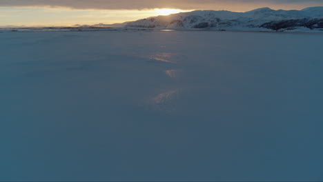 Sunset-over-snow-covered-mountains-in-Iceland-during-winter-drone-tilt-up-shot