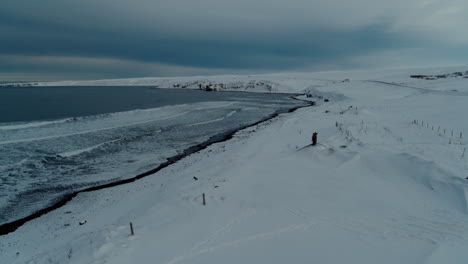 Stehend-An-Einem-Schneebedeckten-Strand-Und-Kontrolliert-Die-Gefrorene-Brandung-In-Island-Im-Winter,-Aufgenommen-Mit-Einer-Drohne