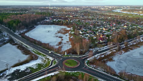 Aerial-drone-shot-flying-high-over-a-a-road-crossing-with-the-view-of-a-town-in-the-background-on-a-cold-winter-day