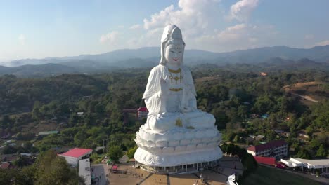 Aerial-circling-around-Wat-Huay-Pla-Kang-giant-white-big-statue-and-pagoda-temple-with-mountains-and-landspace-in-Chiang-Rai,-Thailand