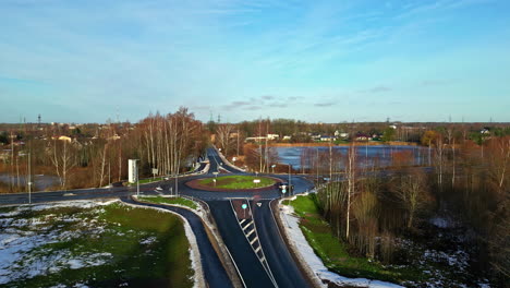Aerial-drone-forward-moving-shot-over-road-crossing-surrounded-by-patches-of-snow-on-a-cold-winter-morning