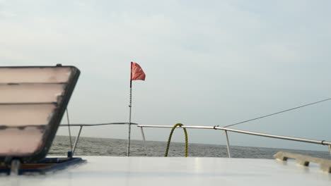 Kleines-Fischerboot-Mit-Einer-Roten-Flagge-An-Der-Vorderseite-Segelt-An-Einem-Trüben,-Bewölkten-Tag-Auf-Rauer-See