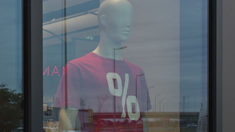 Mannequin-with-red-percentage-discount-t-shirt-in-clothing-store-shopwindow,-handheld-footage