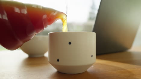 Pouring-fresh-coffee-into-a-mug-beside-a-laptop-and-breakfast-bowl