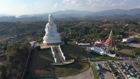 Aerial-drone-of-Wat-Huay-Pla-Kang-giant-white-big-statue-and-pagoda-temple-with-mountains-in-Chiang-Rai,-Thailand