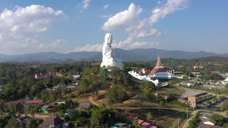 Amazing-aerial-drone-flying-towards-Wat-Huay-Pla-Kang-giant-white-big-statue-and-pagoda-temple-with-mountains-and-landspace-in-Chiang-Rai,-Thailand