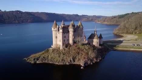 drone-shot-around-chateau-de-val,-french-castle-on-the-shore-of-the-artificial-lake-of-bort-les-les-orgues-on-a-sunny-day-during-winter,-Cantal-departement,-auvergne-rhone-alpes-region,-france