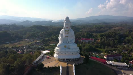 Aerial-of-Wat-Huay-Pla-Kang-giant-white-big-statue-and-pagoda-with-mountains-and-landspace-in-Chiang-Rai,-Thailand
