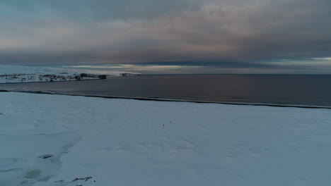 Caminando-Por-La-Nieve-Para-Llegar-A-La-Costa-De-Islandia-Durante-El-Invierno-Filmado-Con-Un-Dron