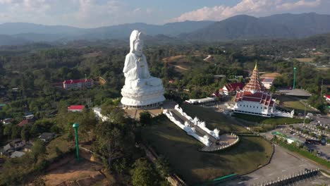 Aerial-drone-of-Wat-Huay-Pla-Kang-giant-white-big-statue-and-pagoda-temple-with-mountains-and-landspace-in-Chiang-Rai,-Thailand
