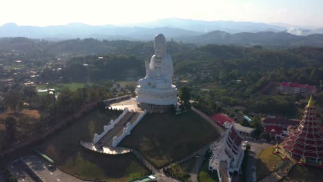 Aerial-drone-of-Wat-Huay-Pla-Kang-huge-white-big-statue-and-pagoda-temple-with-mountains-and-landspace-in-Chiang-Rai,-Thailand