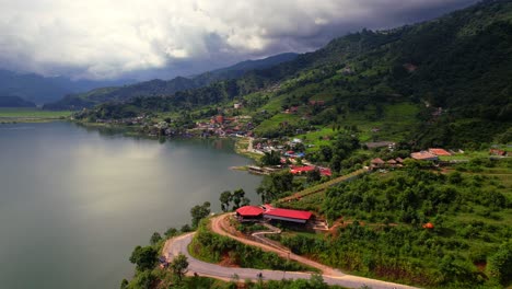 Breathtaking-aerial-landscape-of-Phewa-Lake-with-a-village-on-the-lakeside-and-mountain-scenery,-drone-flying-forward-in-Pokhara,-Nepal
