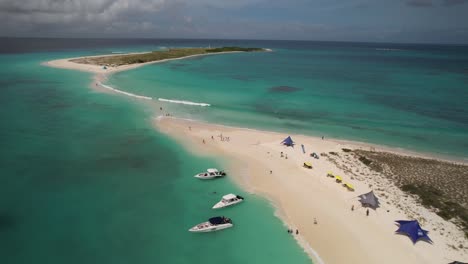 Los-Roques-archipelago-in-Venezuela-with-clear-turquoise-waters,-boats,-and-beachgoers-under-colorful-umbrellas,-aerial-view