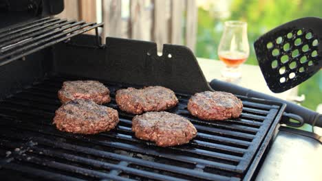 Hamburger-patties-sizzling-on-grill-with-glencairn-glass-of-whisky-bourbon-whiskey-near-water