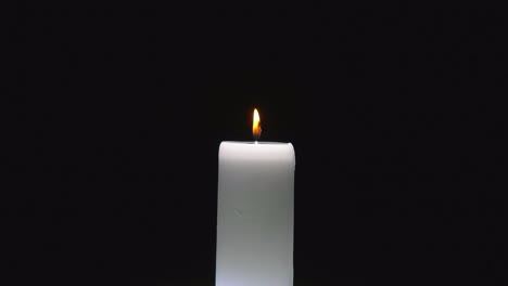 Small-red-flame-flickers-from-white-cylindrical-candle-rotating-as-wax-pools-and-drips-on-black-background