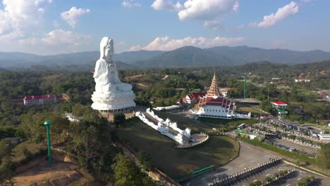 Drone-Aéreo-Volando-Hacia-Wat-Huay-Pla-Kang-Gigante-Estatua-Blanca-Y-Templo-Pagoda-Con-Montañas-Y-Espacio-Terrestre-En-Chiang-Rai,-Tailandia