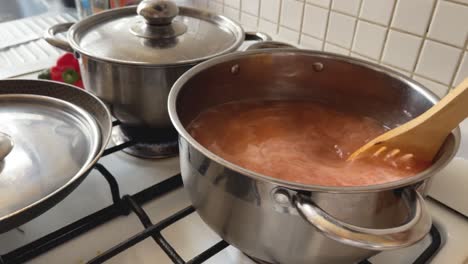 Stir-tomato-soup-with-a-wooden-spoon,-cooked-in-a-steel-pot-on-a-gas-stove