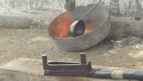 Molten-lead-being-poured-in-a-metal-ladle-at-a-workshop,-dusty-environment,-close-up