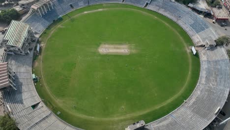 Drone-zoom-out-shot-of-players-playing-cricket-in-stadium-of-Gujranwala-during-daytime-in-Punjab,-Pakistan