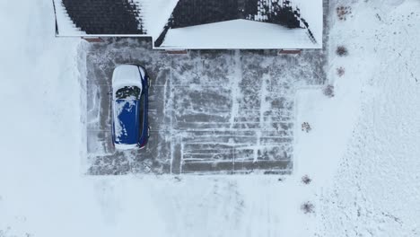 Top-down-aerial-shot-of-a-car-covered-in-snow-sitting-in-a-suburban-driveway