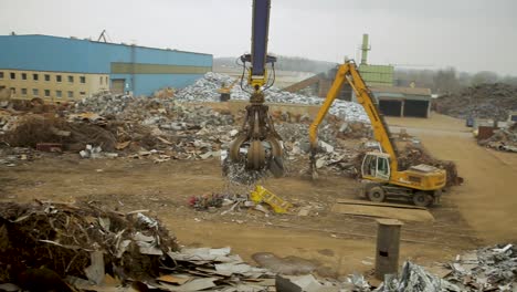 Claw-crane-at-a-scrapyard-lifting-metal-debris,-overcast-day