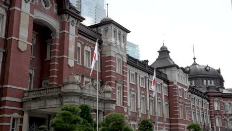 Edificio-Icónico-Con-Su-Fachada-Clásica-De-La-Estación-De-Tren-En-El-Distrito-Comercial-De-Marunouchi-En-Chiyoda,-Tokio,-Japón,-Con-Banderas-Rodeándola