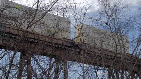 Intermodal-Freight-Train-Crosses-the-Pope-Lick-Trestle-in-Louisville,-KY,-Behind-some-Bare-Trees-on-a-Cloudy-Morning