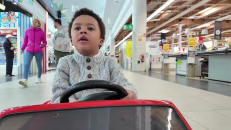 Liebevolles-Und-Lustiges-3-jähriges-Schwarzes-Kind,-Das-In-Einem-Einkaufszentrum-Ein-Elektrisches-Spielzeugauto-Fährt