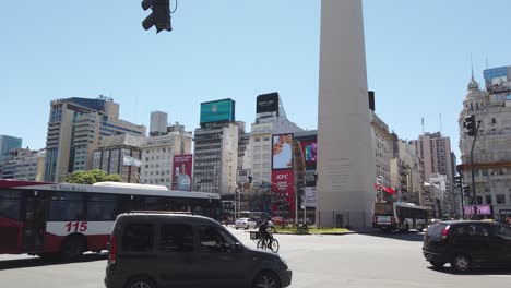 Cars,-Buses-and-Taxis-Drive-at-9-of-July,-Obelisk-and-Corrientes-Avenue,-City-Landmark-during-Vibrant-Summer-Morning,-Skyline-and-Business-Downtown