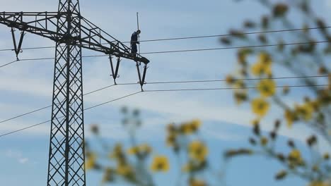 Worker-on-high-voltage-power-line-against-blue-sky,-safety-harness,-clear-day