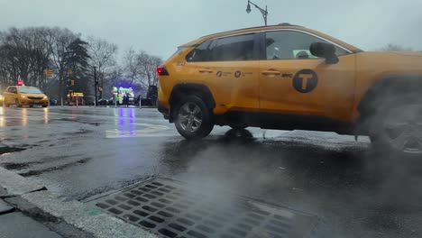 A-low-angle-view-of-NYC-yellow-taxi's-driving-by-a-sewer-drain-emitting-steam-on-a-cloudy-and-wet-day
