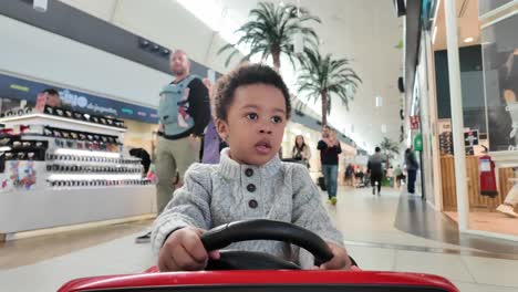 Cute-and-exotic-3-year-old-black-kid-riding-a-red-electric-toy-car-inside-a-Mall